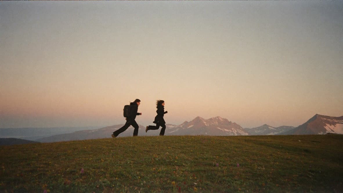 Two silhouettes running along a mountain ridge at dawn